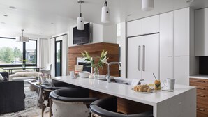 Una cocina moderna con una isla central, taburetes de bar, un televisor de pantalla plana y un amplio ventanal con vistas al exterior.