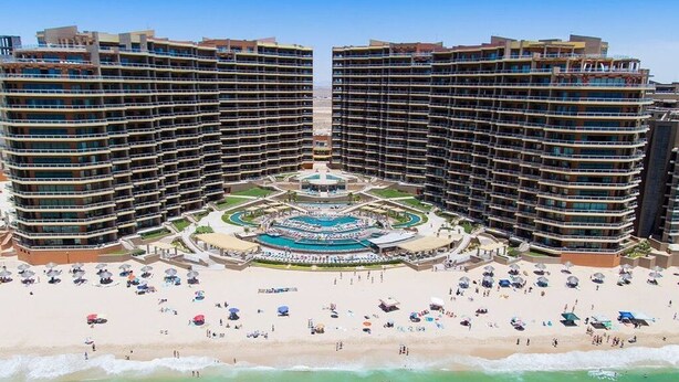 Un hôtel de grande hauteur doté d’une cour intérieure, de nombreux balcons et d’un espace plage avec des parasols.