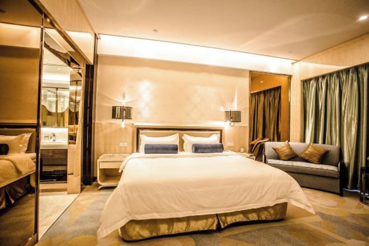 Une chambre d’hôtel avec un grand lit, des tables de chevet, un canapé, un miroir et des rideaux.