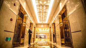 Un vestíbulo de hotel con piso de mármol reflectante, una lámpara de araña grande y paredes espejadas.