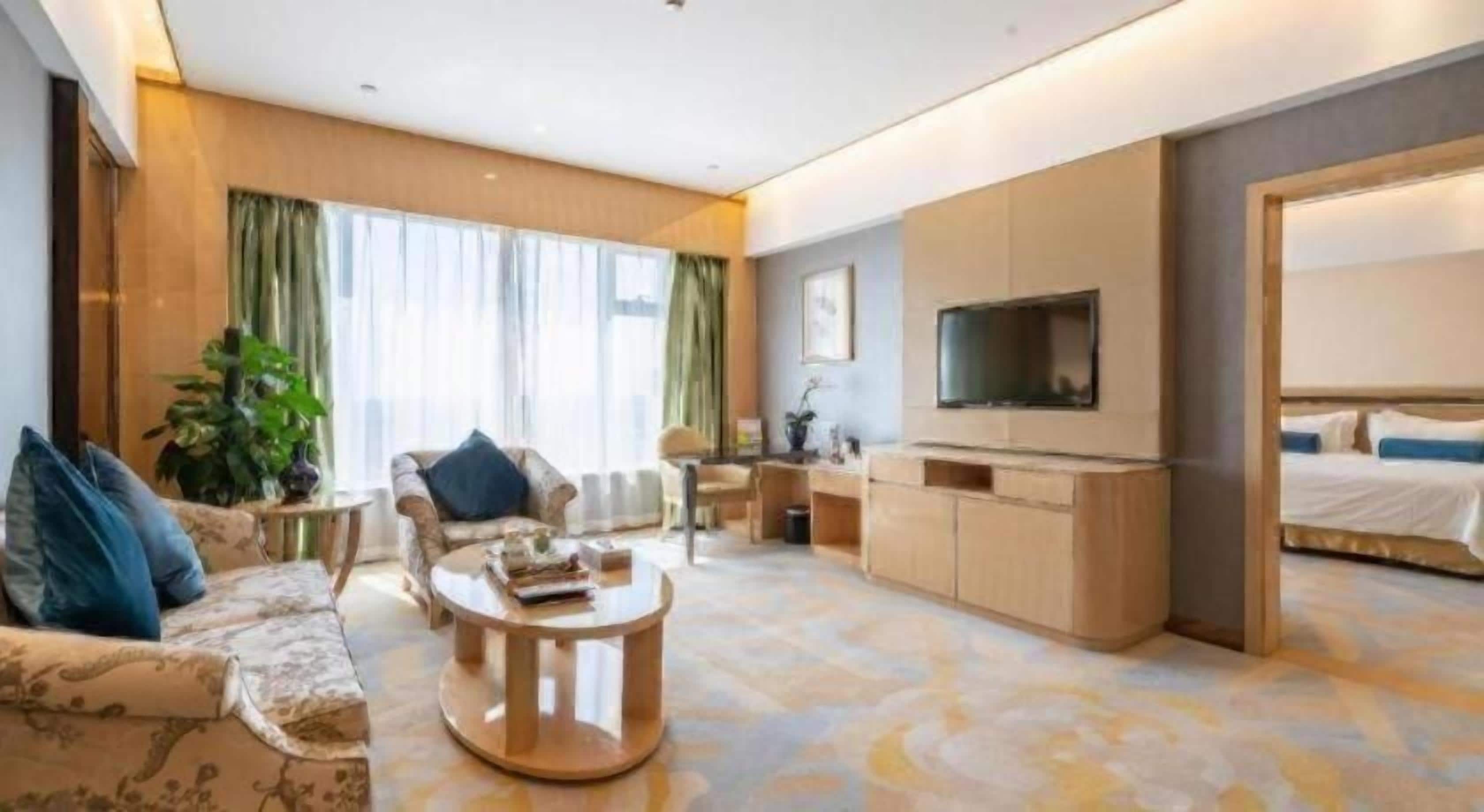 Una habitación de hotel moderna con un conjunto de sofás, una mesa de centro, un televisor y una cama.