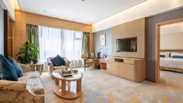 Una habitación de hotel moderna con un conjunto de sofás, una mesa de centro, un televisor y una cama.