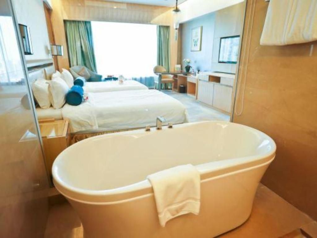 Quarto de hotel com uma banheira grande, uma cama com almofadas, uma escrivaninha e uma televisão.