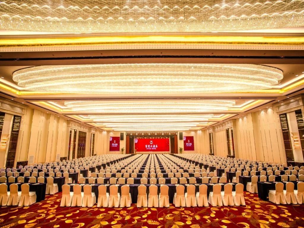 Un salón de conferencias con filas de sillas, un escenario con fondo rojo y una alfombra estampada.