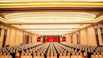 Un salón de conferencias con filas de sillas, un escenario con fondo rojo y una alfombra estampada.