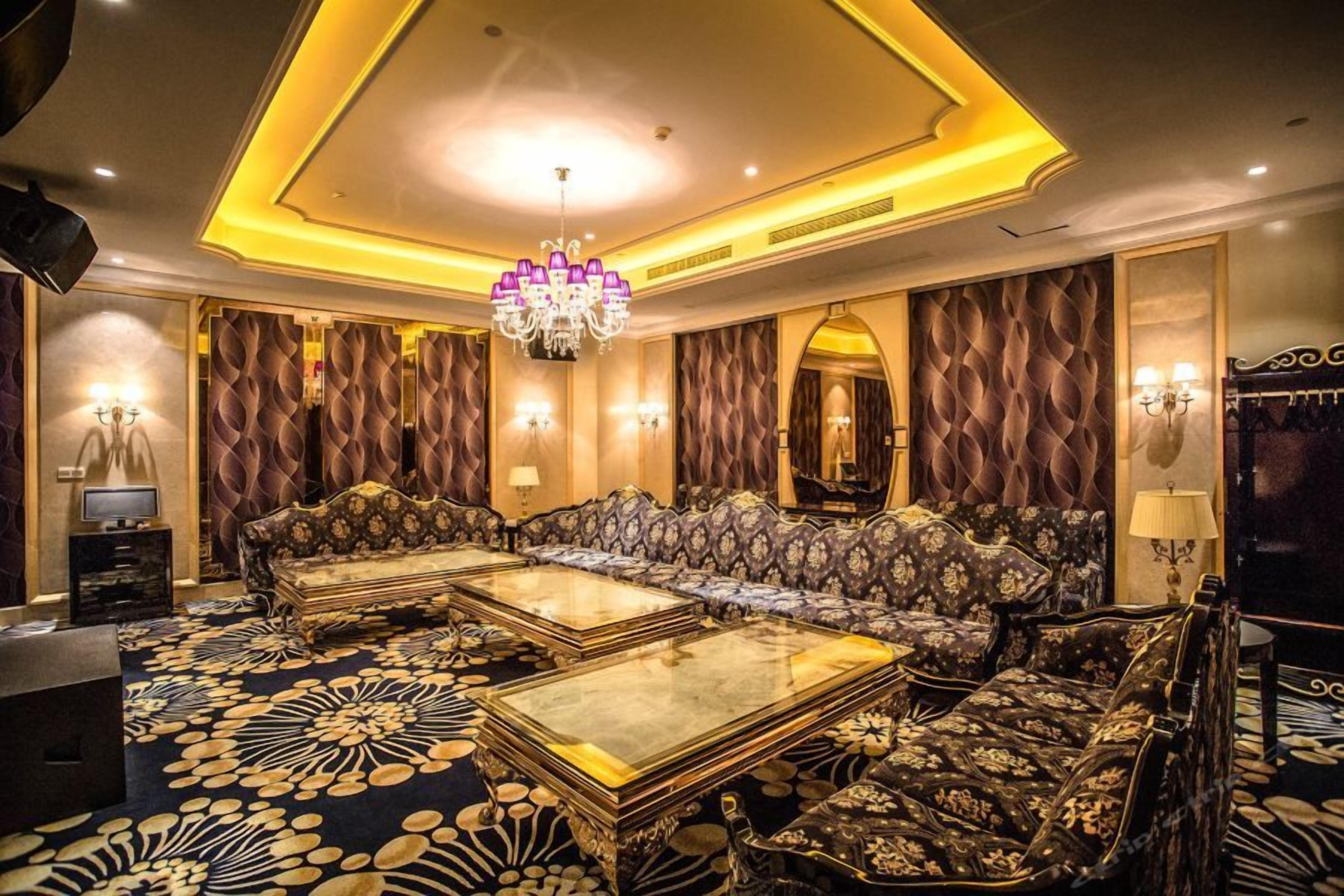 Een luxe kamer met een zithoek, twee bijzettafels, een kroonluchter en een kamerbreed tapijt met dessin.