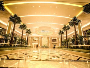 Un hall d’entrée spacieux avec un plafond haut, des palmiers et un élément décoratif central.