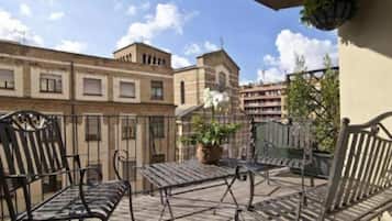 Un balcón con una mesa y sillas, una planta en maceta y vistas a edificios.