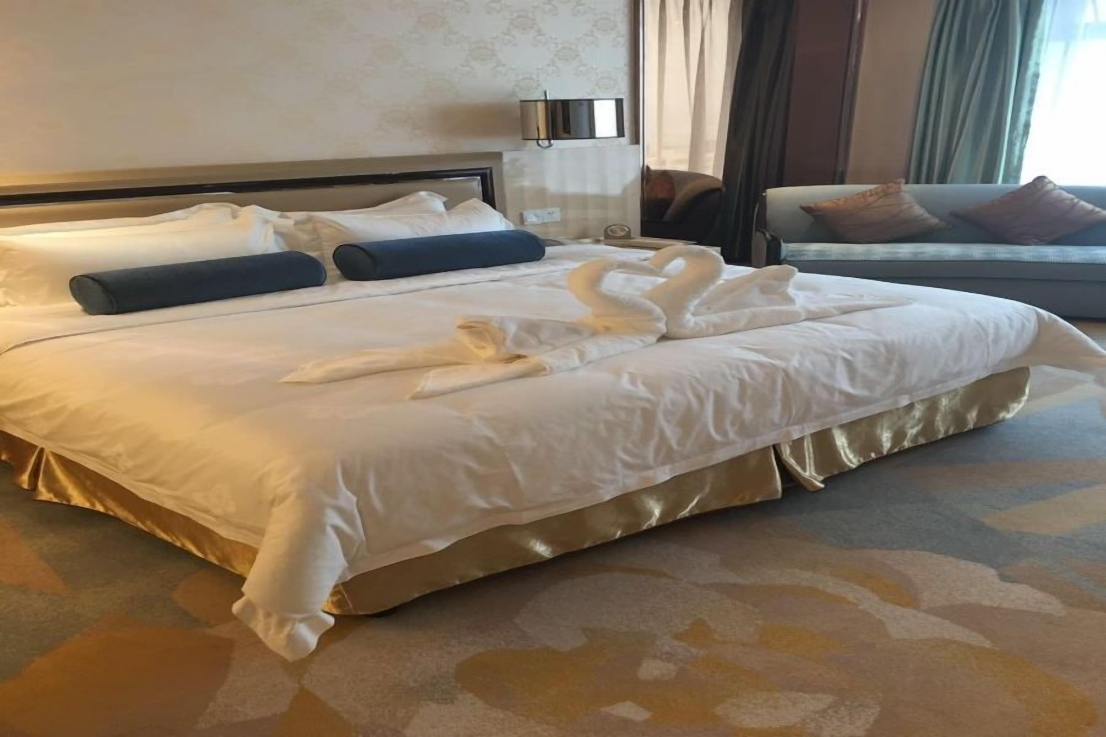 Quarto de hotel com uma cama grande, um sofá e uma luminária fixada na parede.