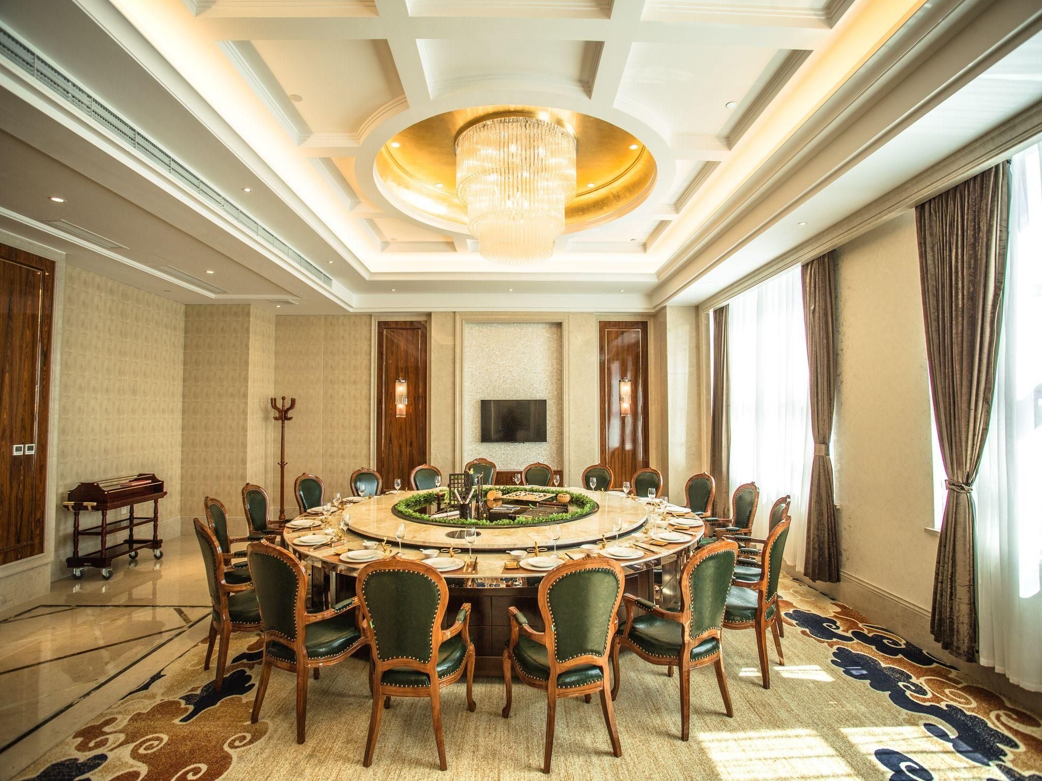 Uma sala de jantar formal com uma mesa redonda, cadeiras, um lustre e uma janela grande.