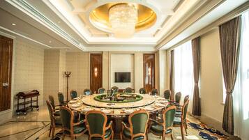 Uma sala de jantar formal com uma mesa redonda, cadeiras, um lustre e uma janela grande.