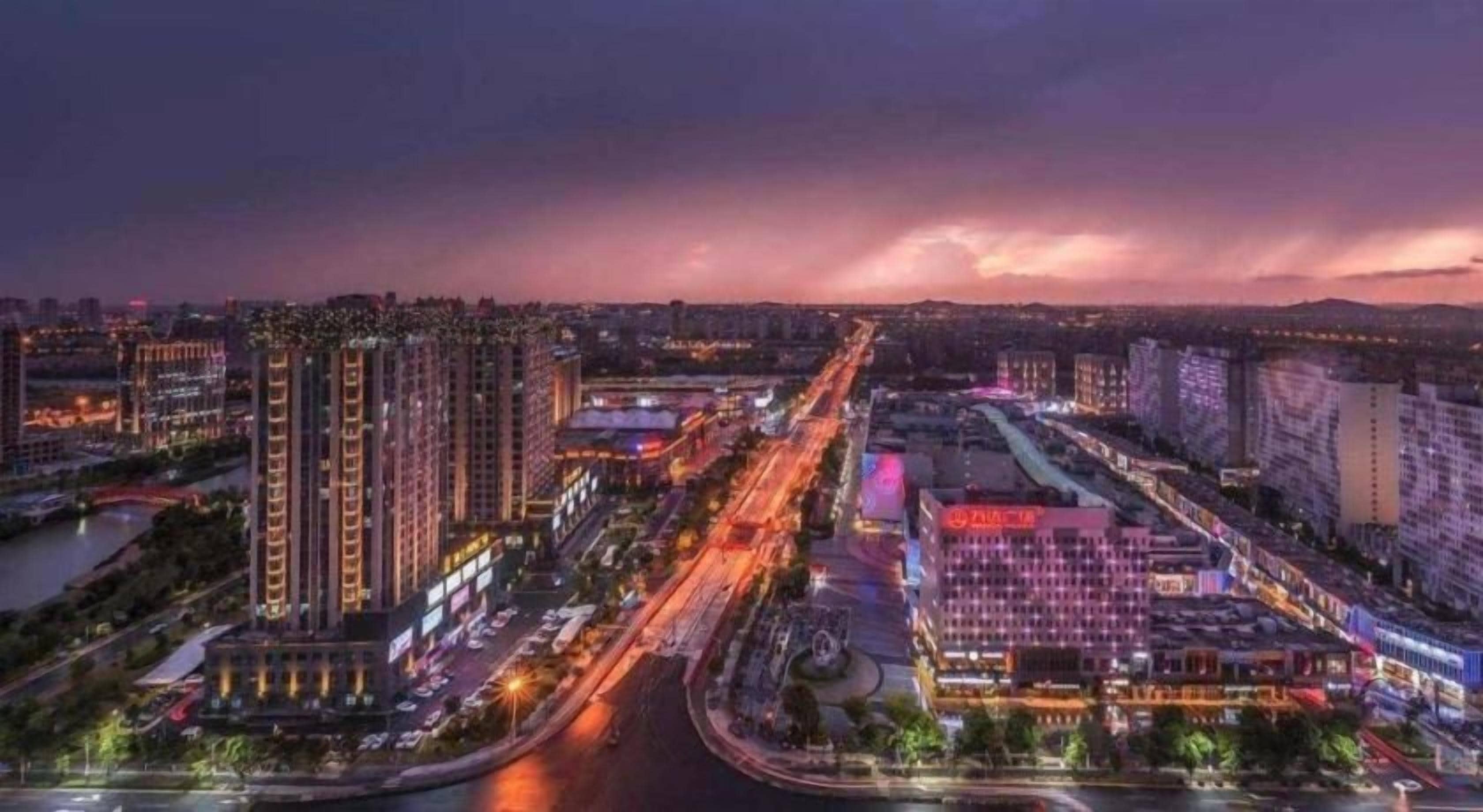 A cityscape at dusk with illuminated buildings and a river.
