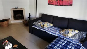 A living room with a black sofa, patterned cushions, a fireplace, a floor lamp, and a painting of flowers on the wall. - Lisbon Coast (Costa da Caparica)