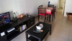 A living room with a TV, a bookshelf, a dining table with chairs, and a coffee table. - Lisbon Coast (Costa da Caparica)