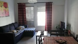 A living room with a sofa, a dining table with chairs, a TV, and a ceiling fan. - Lisbon Coast (Costa da Caparica)