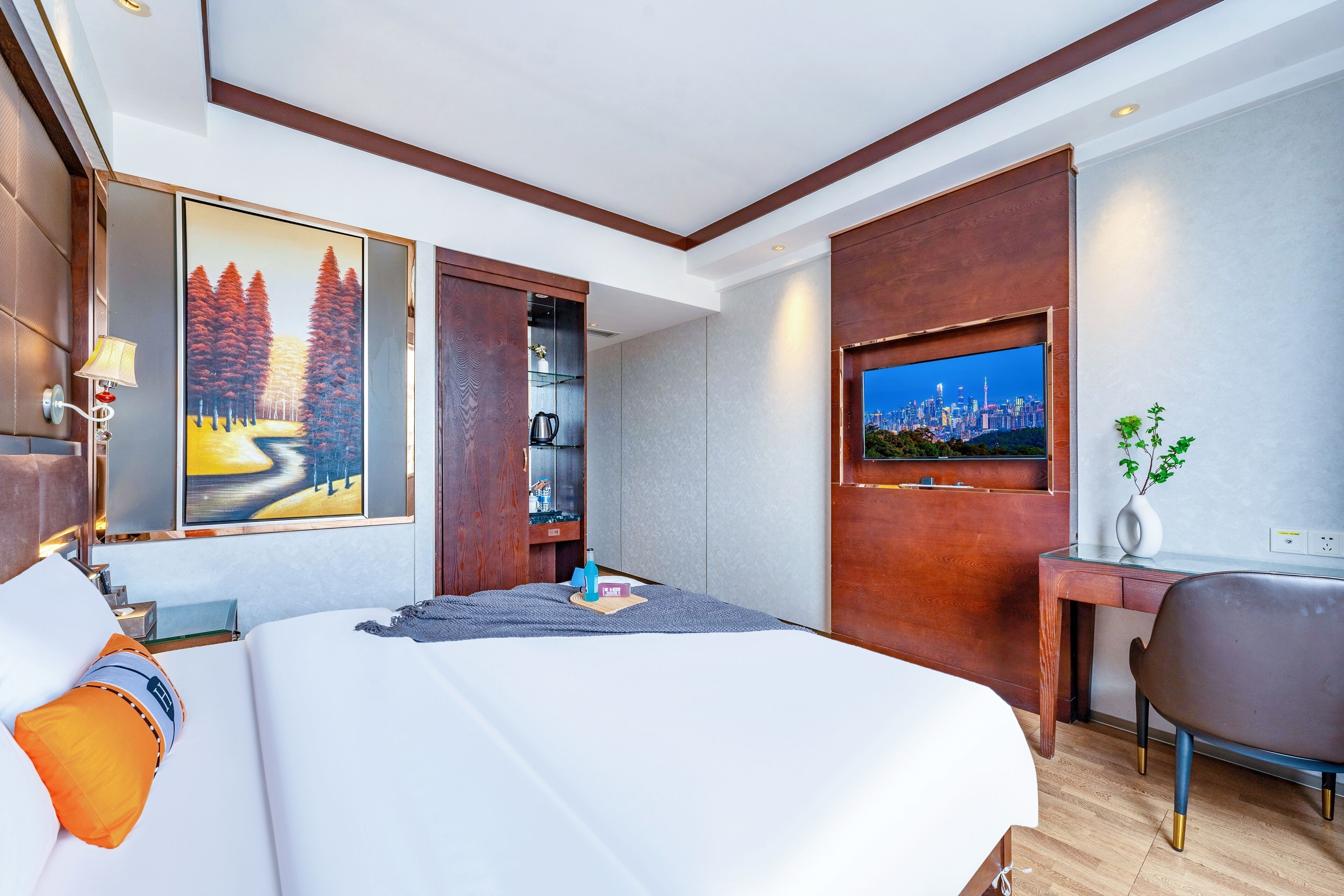 Habitación de hotel con una cama grande, un escritorio, un televisor y un cuadro de un bosque.