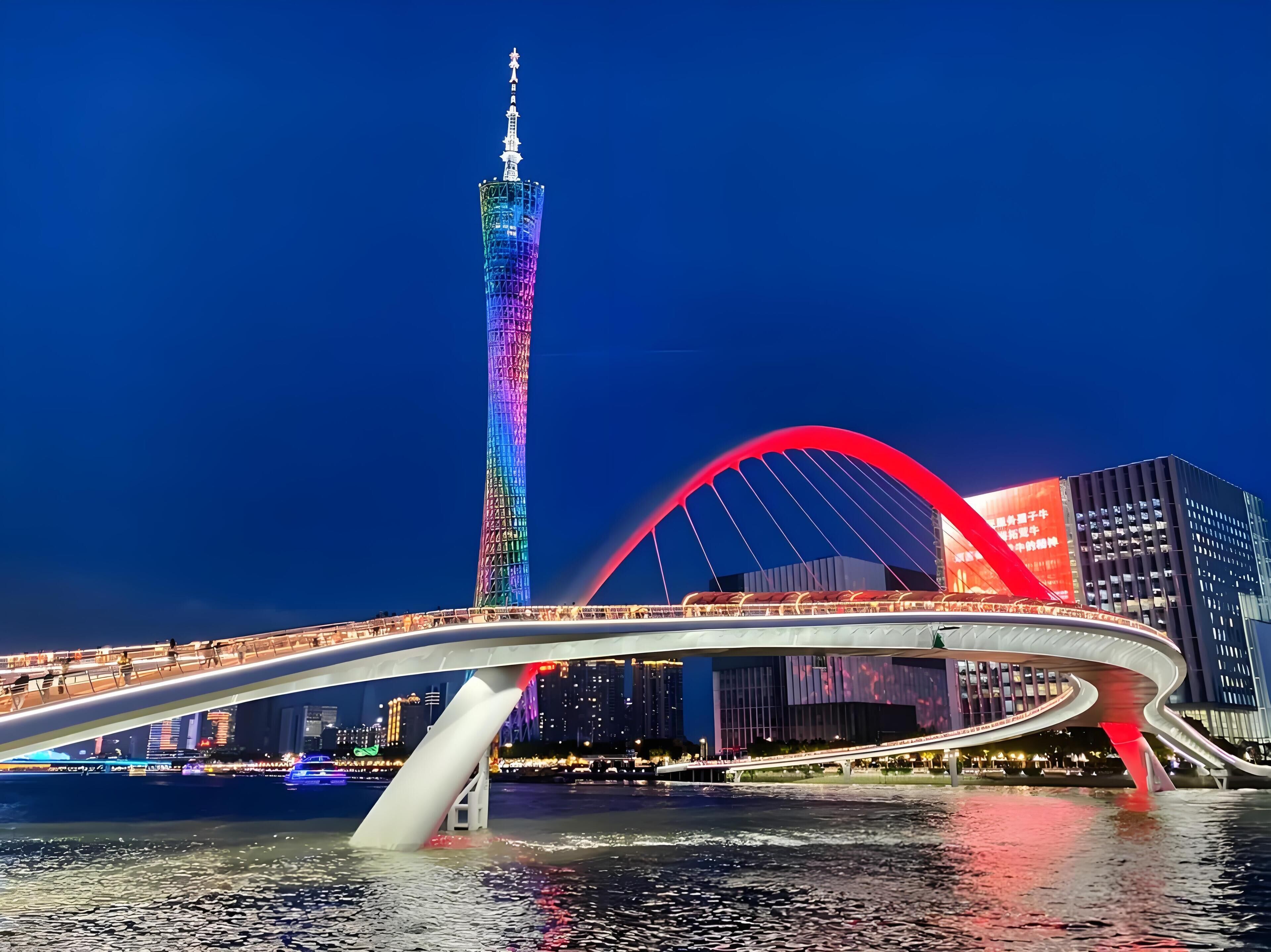 Un pont moderne à l’architecture audacieuse, avec un arc distinctif, une haute tour illuminée en arrière-plan et une étendue d’eau en contrebas.