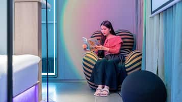 A person sitting on a striped bean bag chair reading a book in a room with a modern design, including a wooden cabinet and a floor lamp.