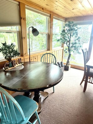 A wooden interior with a round table, chairs, and a large window.
