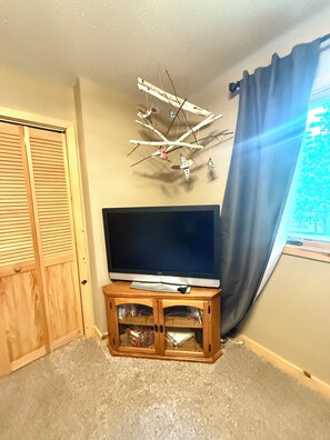 A room with a television on a wooden stand, a wooden wardrobe, and a wall-mounted decoration.