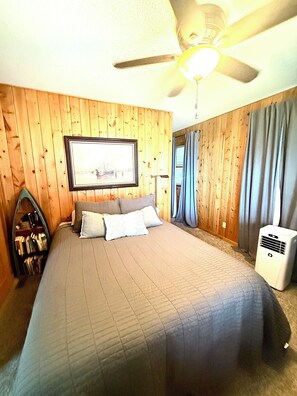 A bedroom with a bed, a ceiling fan, a mounted TV, and a heater.