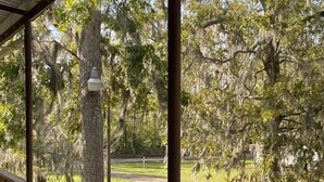 A wooden deck with a railing overlooking a grassy area with trees and a car parked nearby. - Three Mile Lake -WATERFRONT and completely Furnished lake house . (Port Barre)