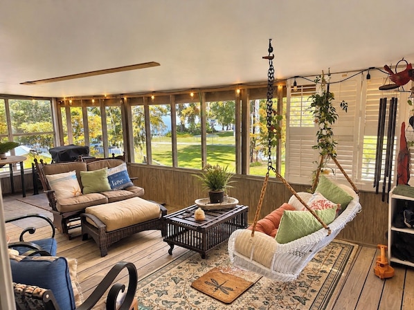 Un solarium con un sofá, sillas, una mecedora colgante y vistas a un paisaje verde.