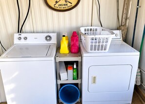Une buanderie équipée de deux machines à laver et deux sèche-linge, d’une horloge et de divers produits de lessive.