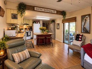A cozy living room with a leather sofa, a dining area with a bar, and a kitchen with wooden cabinets. -   Peaceful Waterfront Retreat on Three Mile Lake • Bring Your Boat (Port Barre)