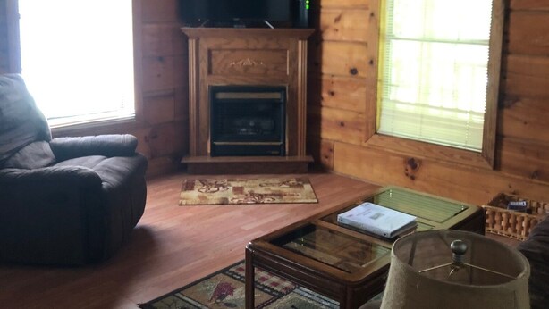L’intérieur d’un chalet en bois chaleureux et accueillant, avec une cheminée, un téléviseur, un fauteuil en cuir et un ventilateur de plafond.