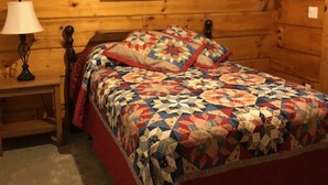 Une chambre à coucher dans une cabane en bois, avec un lit, une table de chevet, une lampe et un tableau encadré au mur.