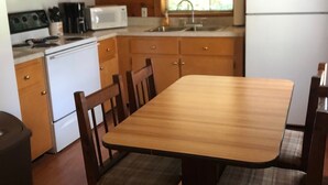 Une cuisine aménagée dans le style d’un chalet en bois, avec une table et des chaises, un fourneau, un four à micro-ondes et un réfrigérateur.