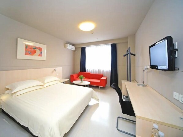 A hotel room with a bed, a desk with a computer, a red sofa, and a window with curtains. - Jinjiang Inn (Wuhan)