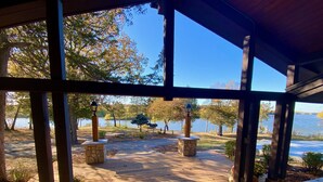 Una terraza techada con vistas a un lago, bancos de piedra y piso de madera.