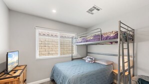 Un dormitorio con literas, una ventana con persianas, un televisor sobre un soporte de madera y suelo alfombrado.