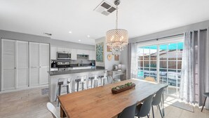 Una cocina moderna con una isla central, muebles blancos y un comedor con mesa y sillas de madera.