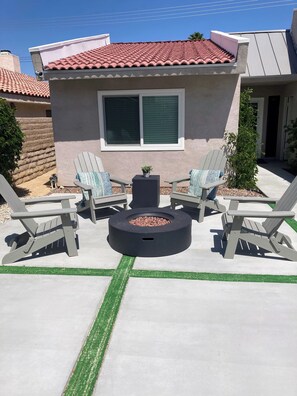 A patio area with Adirondack chairs, a round fire pit, and a small potted plant.