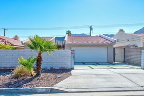 A residential property with a garage, a gated driveway, and a landscaped area with palm trees.
