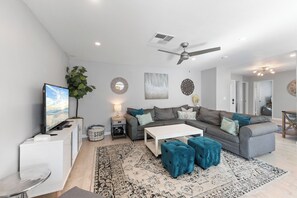 A modern living room with a grey sofa, a coffee table, a TV, and a ceiling fan.