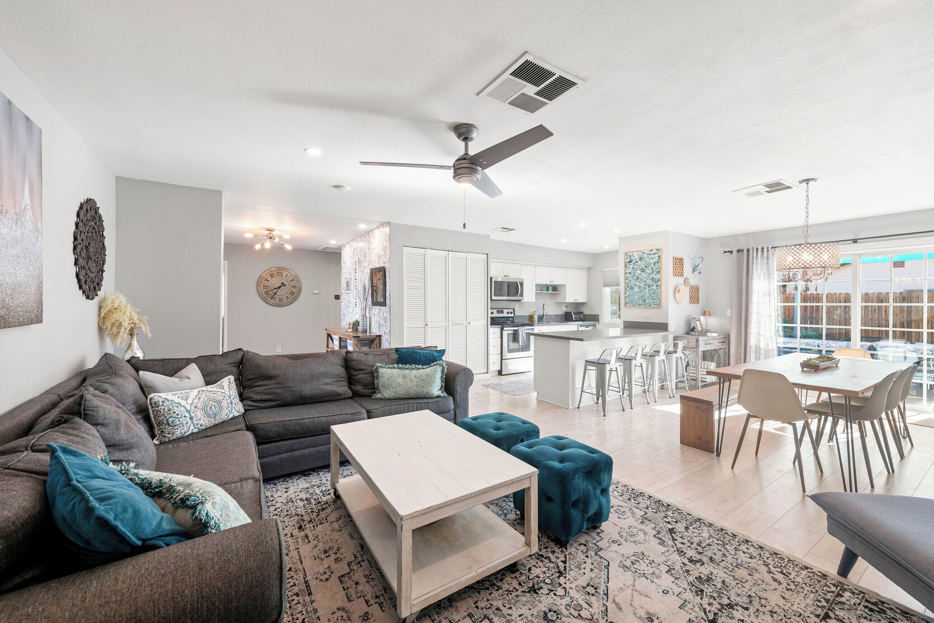 A modern living room with a sofa, ottoman, and coffee table. There is a kitchen area with a dining table and chairs.