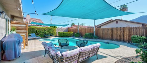 A backyard with a swimming pool, covered seating, and a wooden fence.