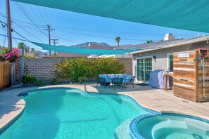 Un patio trasero con piscina, zona de barbacoa cubierta y terraza amueblada.
