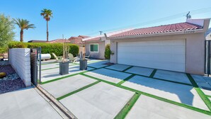 Una propiedad residencial con garaje, camino de entrada pavimentado con bordes de césped verde y una palmera.