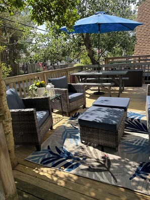 Un patio exterior con muebles de mimbre, un paraguas azul y una terraza de madera.