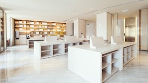 A modern hotel lobby with a central reception desk, a large bookshelf, and a sleek elevator. - Ji Hotel (Shanghai)