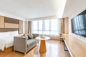 A modern hotel room with a bed, sofa, round table, and a TV on the wall. - Ji Hotel (Shanghai)