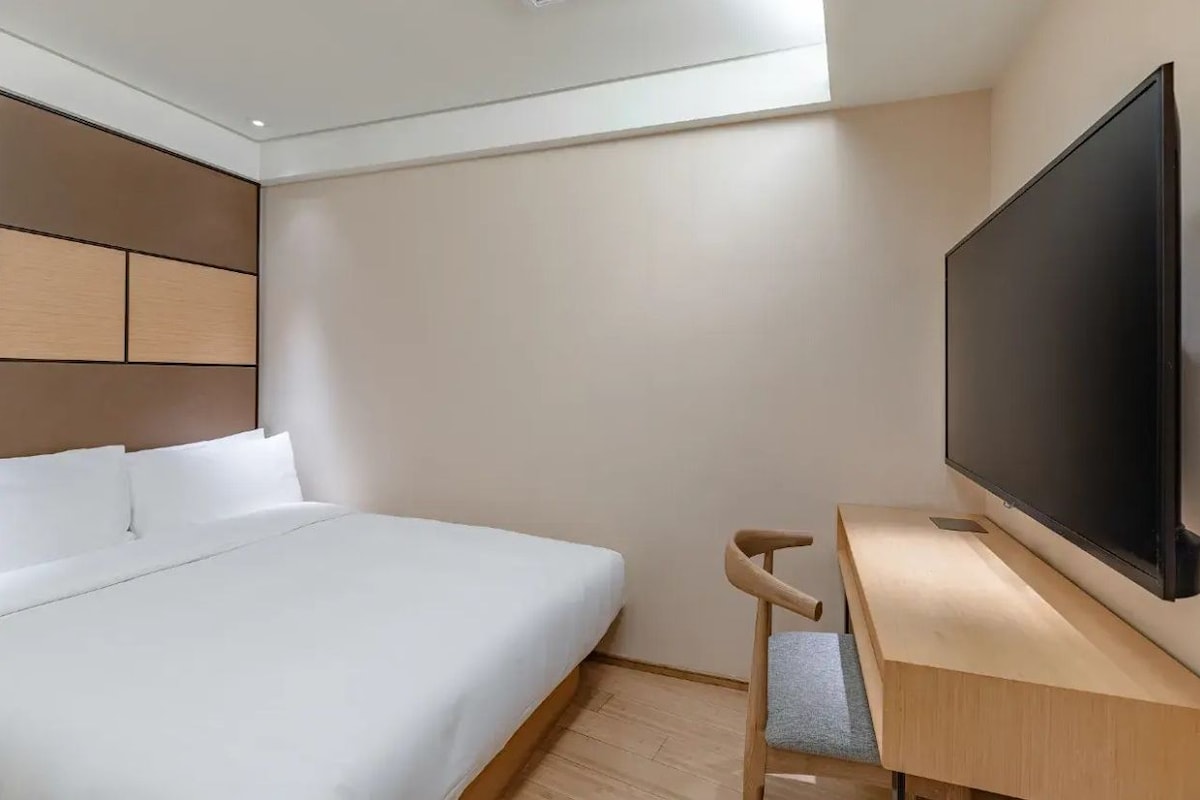 A hotel room with a bed, a desk with a flat-screen TV, and a wall-mounted TV.
