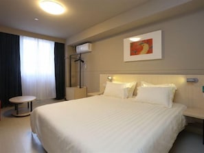A hotel room with a large bed, a bedside table, a chair, a window with curtains, and an air conditioning unit. - Jinjiang Inn (Chengdu)