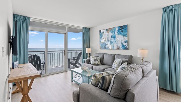 A living room with a sofa, a coffee table, and a view of the ocean through a sliding glass door.