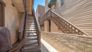 A narrow alleyway with a wooden staircase leading to a building with a stone wall and a metal railing.